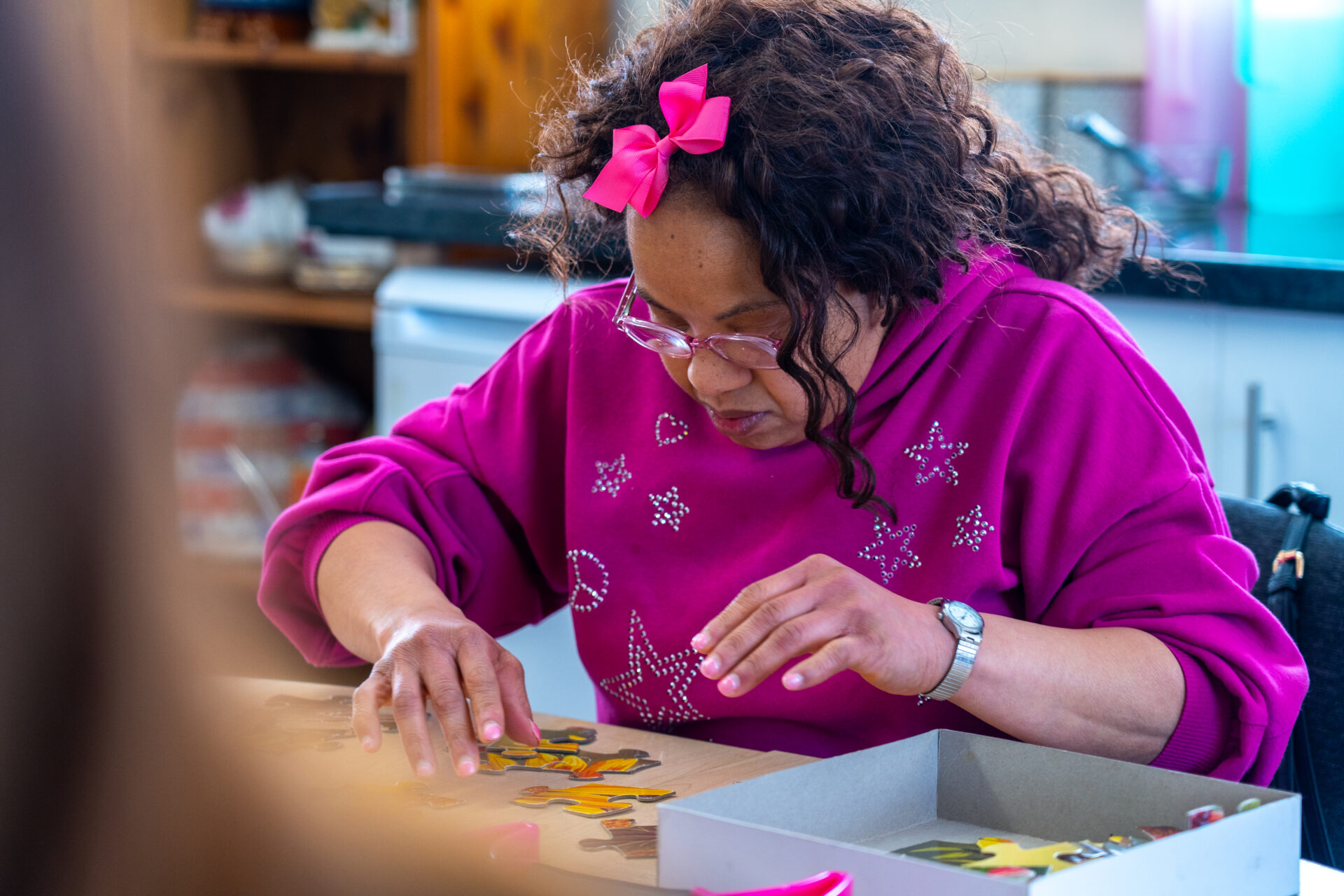 A woman in a pink jumper enjoying a jigsaw