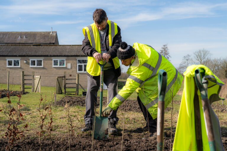 Two volunteers in high-vis jackets digging with spades