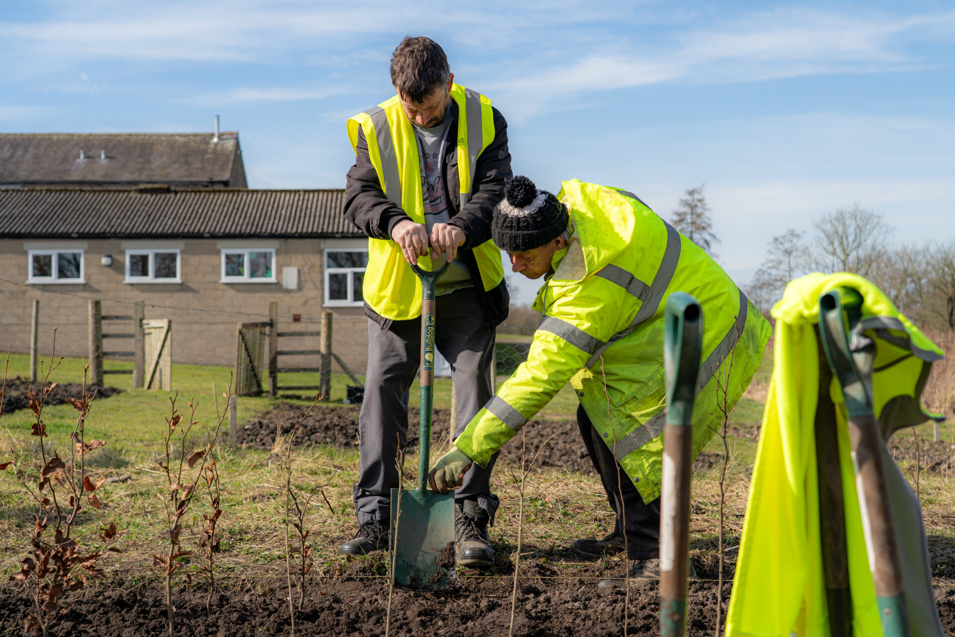 Two volunteers in high-vis jackets digging with spades