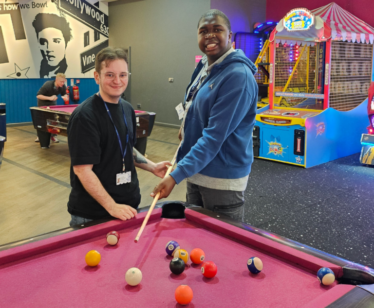 Two adults smiling while playing pool in a leisure centre