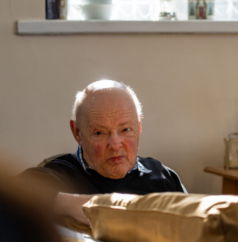 An old man looking over the back of a sofa