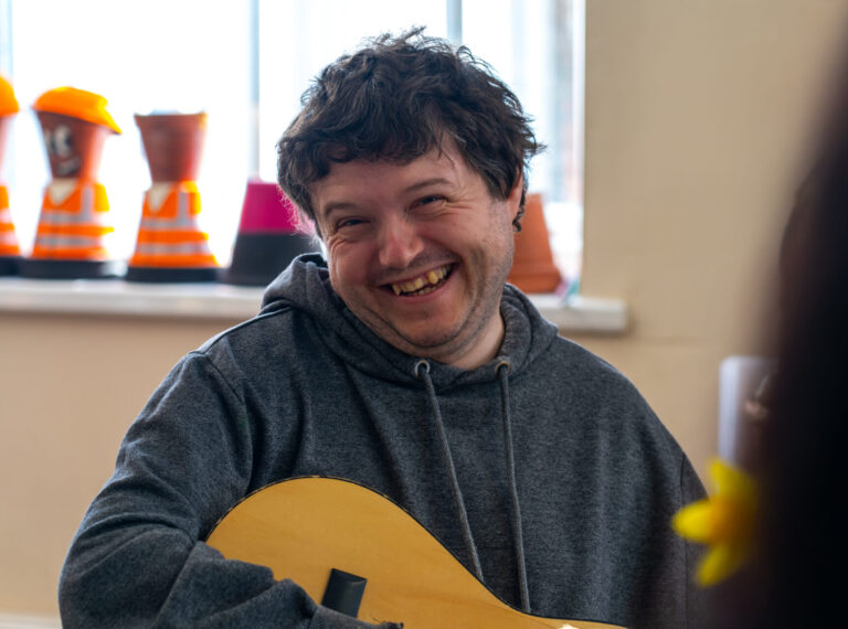 Man smiling while playing a guitar during a music session