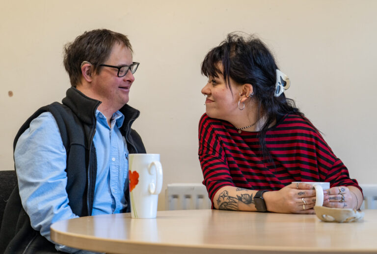 A man and a woman sitting at a table talking to each other and enjoying beverages