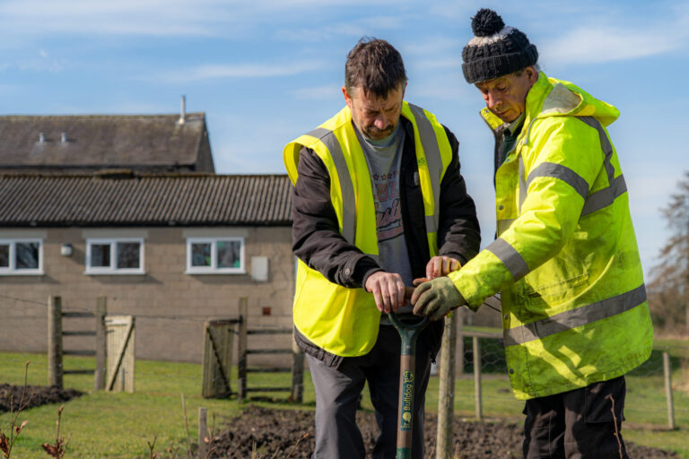 two men in yellow high-vis holding a shovel at Best Lives, a leading social care provider