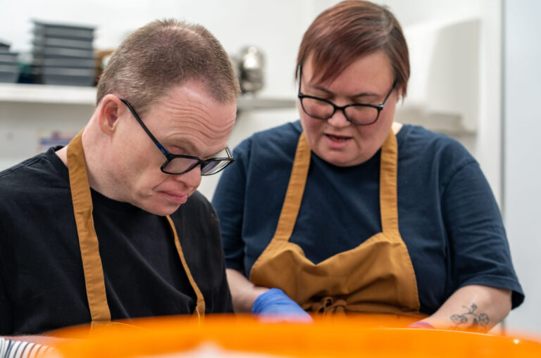 Photo of a support worker supporting a man at Roccoco Cafe with food prep