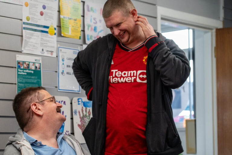 a man in a red shirt laughing with his hand on his neck