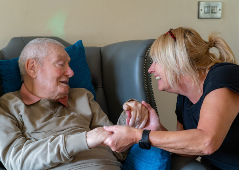 Support worker smiling while holding hands with an older adult