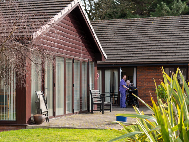 a woman standing outside of a nursing home pushing a wheelchair
