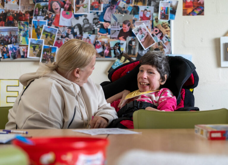 Woman smiling with an adult in a wheelchair in front of a collage display