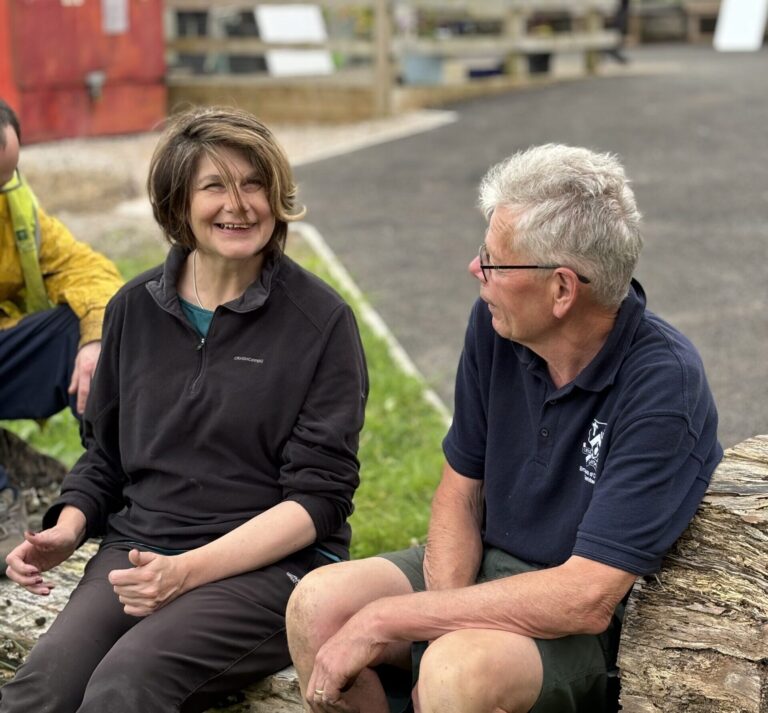 Two adults smiling and talking while sitting outdoors