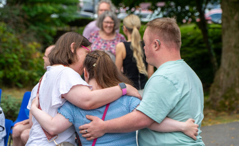 Three people hugging each other at a summer party. Brothers of Charity Services rebrand