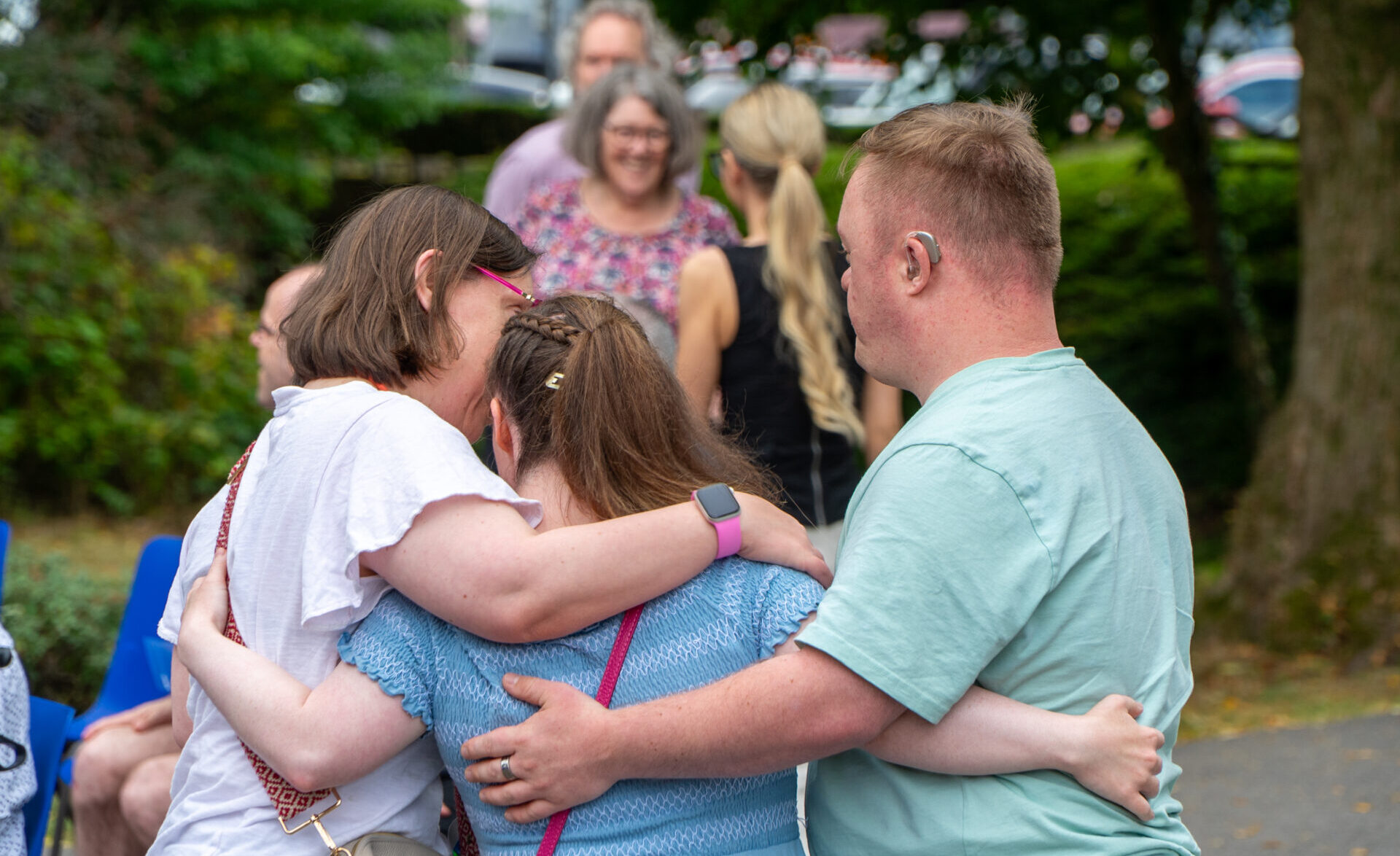 Three people hugging each other at a summer party. Brothers of Charity Services rebrand
