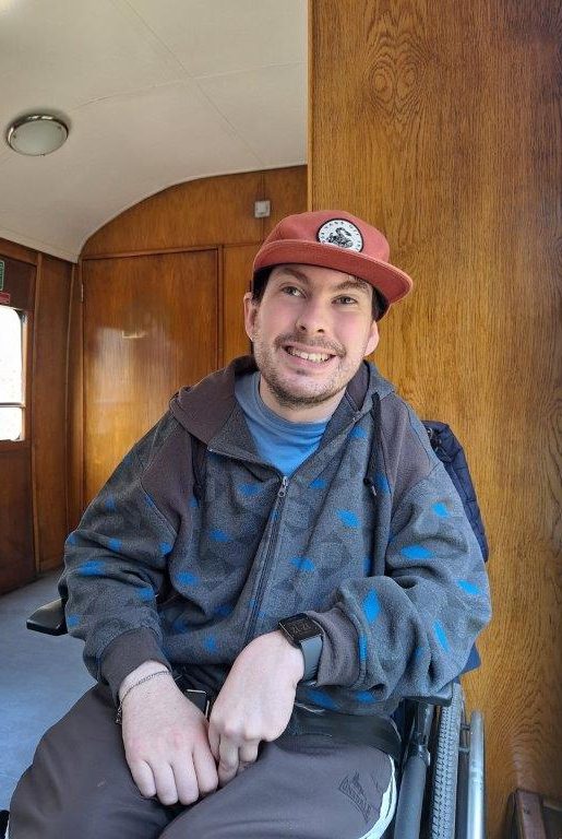 Man in wheelchair wearing blue clothes and red cap, smiling